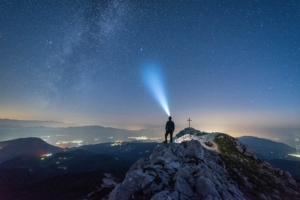 Man on mountain using night headlamp to see the night sky.